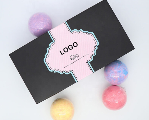 Minimalist black bath bomb packaging with logo branding – A sleek black box wrapped in a pink and blue accent band, with neatly arranged bath bombs placed beside it, showcasing elegance and simplicity.