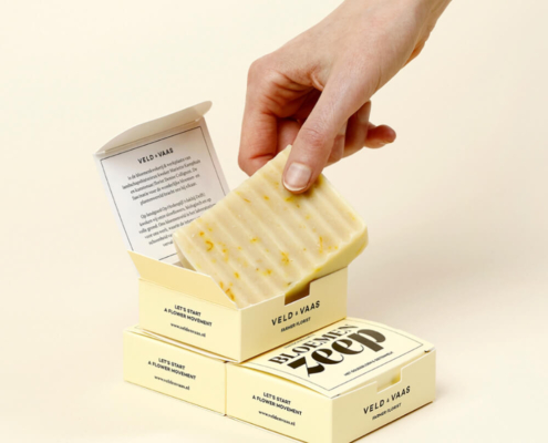 Open soap box packaging revealing the soap bar inside, with a hand lifting it, showcasing interior design for wholesale soap packaging.