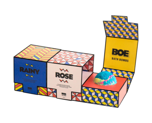 Vibrant bath bomb boxes with geometric patterns and a single bath bomb displayed in the open packaging.