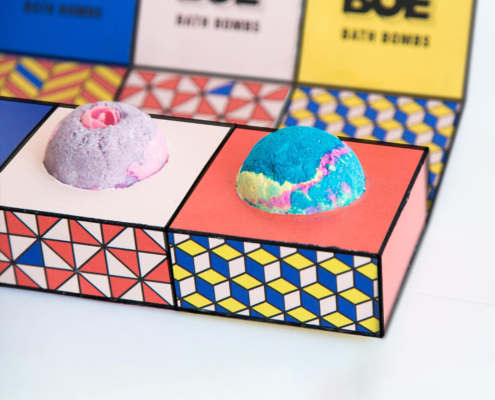 Two bath bombs in colorful custom packaging with vibrant geometric designs.