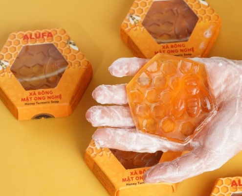 Hand holding a hexagon-shaped soap bar next to matching soap boxes.