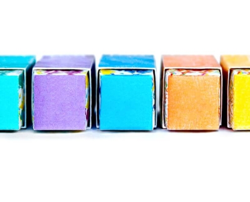 Row of Colorful Custom Lipstick Boxes in Various Shades - Close-up of vibrant lipstick boxes in shades of purple, blue, orange, and yellow, each with a unique patterned base.