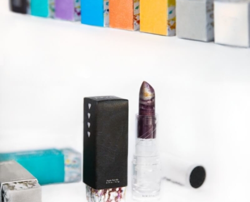 Custom Lipstick Packaging with Lipstick Display - Black lipstick box with heart symbols and an abstract base next to a lipstick, with more colorful boxes in the background.