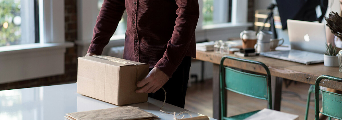 Small business owner wrapping a cardboard box with twine in a modern workspace.