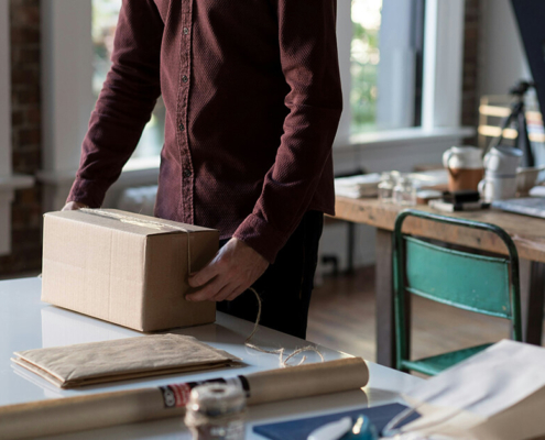 Small business owner wrapping a cardboard box with twine in a modern workspace.